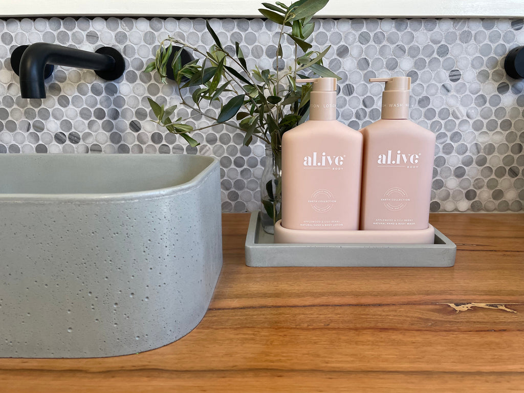 Illy powder concrete basin by DLH Designs in Sage displayed with an Al.ive Body wash and Lotion Duo plus tray in Blush pink